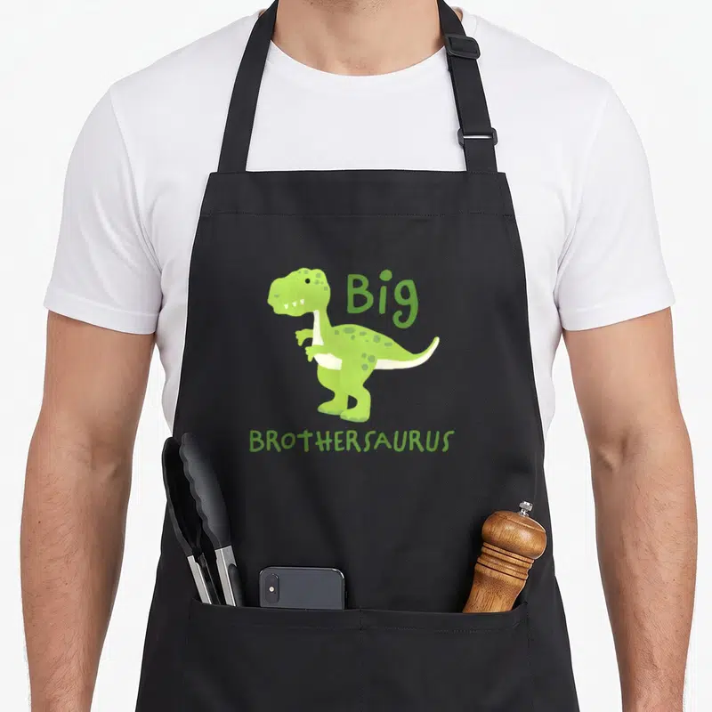 Tablier de cuisine noir avec dinosaure vert et texte Big Brothersaurus imprimé au centre.