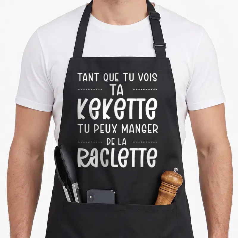 Tablier de cuisine noir avec le texte blanc Tant que tu vois ta kekette tu peux manger de la raclette imprimé en typographie ludique.