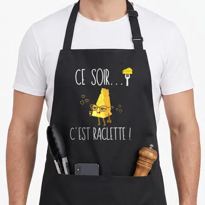 Tablier de cuisine noir avec un fromage aux lunettes tenant une valise et le texte Ce soir c'est raclette.