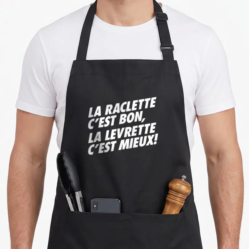 Tablier de cuisine noir avec le texte blanc La Raclette C'est Bon La Levrette C'est Mieux imprimé au centre.