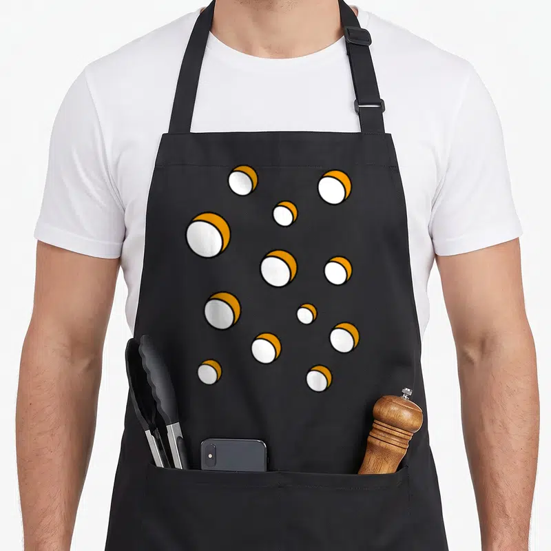 Tablier de cuisine noir avec un motif répétitif de boules blanches et jaunes représentant des fromages fondants stylisés.
