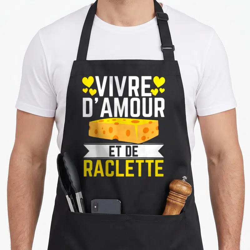 Tablier de cuisine noir avec illustration de bloc de fromage jaune, cœurs et texte Vivre d'amour et de raclette en blanc et jaune.