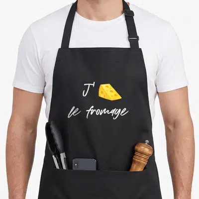 Tablier de cuisine noir avec une illustration de fromage à raclette jaune et un texte blanc manuscrit.