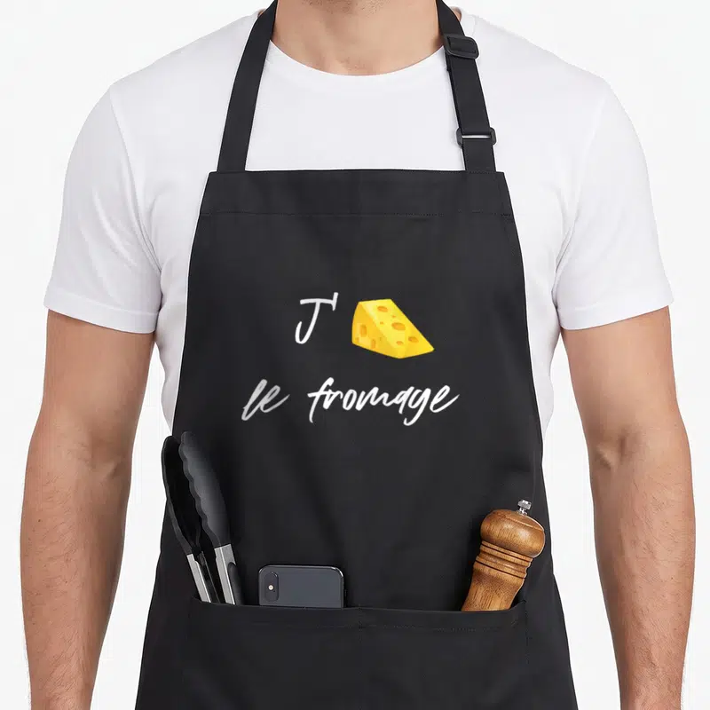 Tablier de cuisine noir avec une illustration de fromage à raclette jaune et un texte blanc manuscrit.