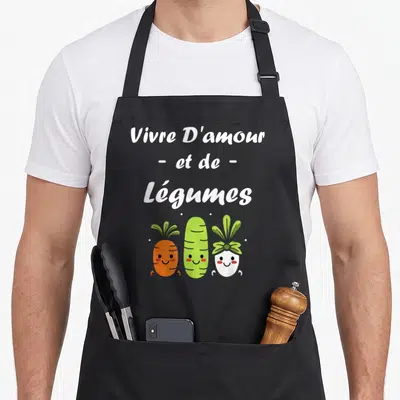 Tablier de cuisine noir avec inscription Vivre D'amour et de Légumes et trois légumes souriants orange vert et blanc.