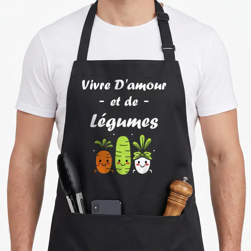 Tablier de cuisine noir avec inscription Vivre D'amour et de Légumes et trois légumes souriants orange vert et blanc.
