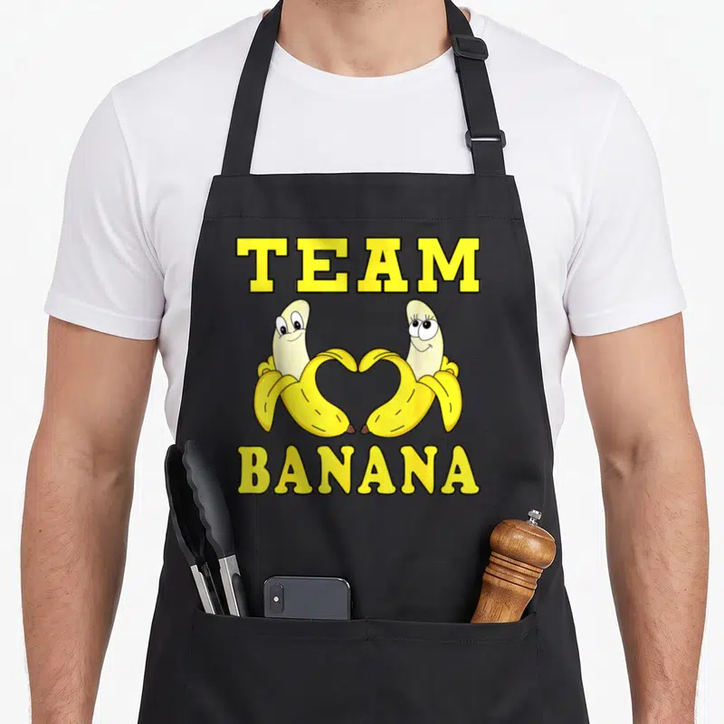 Tablier de cuisine noir avec deux bananes cartoon formant un cœur sous le texte Team Banana en lettres jaunes.