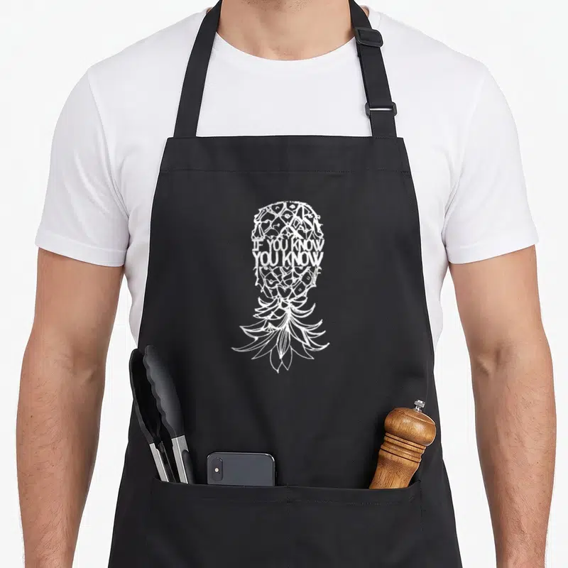 Tablier de cuisine noir avec illustration blanche d'ananas contenant le texte IF YOU KNOW YOU KNOW au centre du motif.
