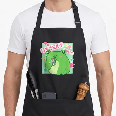 Tablier de cuisine noir avec illustration d'une grenouille verte buvant du lait au carton rose entourée d'étoiles et de cœurs.