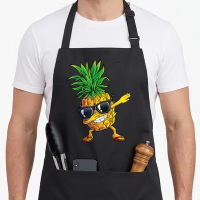 Tablier de cuisine noir avec un ananas anthropomorphisé portant des lunettes noires et effectuant un mouvement de danse moderne.