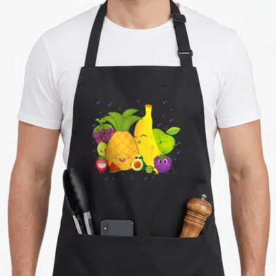 Tablier de cuisine noir avec des fruits anthropomorphes souriants comme un ananas et une banane jaune.