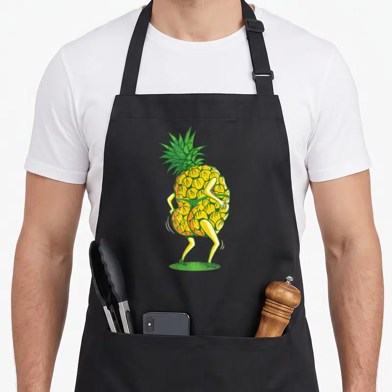 Tablier de cuisine noir avec illustration d'un ananas dansant aux hanches en mouvement et chaussures vertes.