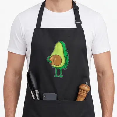 Tablier de cuisine noir avec un avocat vert anthropomorphisé montrant ses fesses en forme de noyau marron.