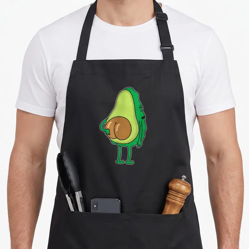 Tablier de cuisine noir avec un avocat vert anthropomorphisé montrant ses fesses en forme de noyau marron.