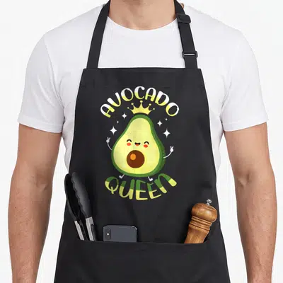Tablier de cuisine noir avec un avocat cartoon souriant portant une couronne dorée et le texte avocado queen guac fruit guacamole avocat.