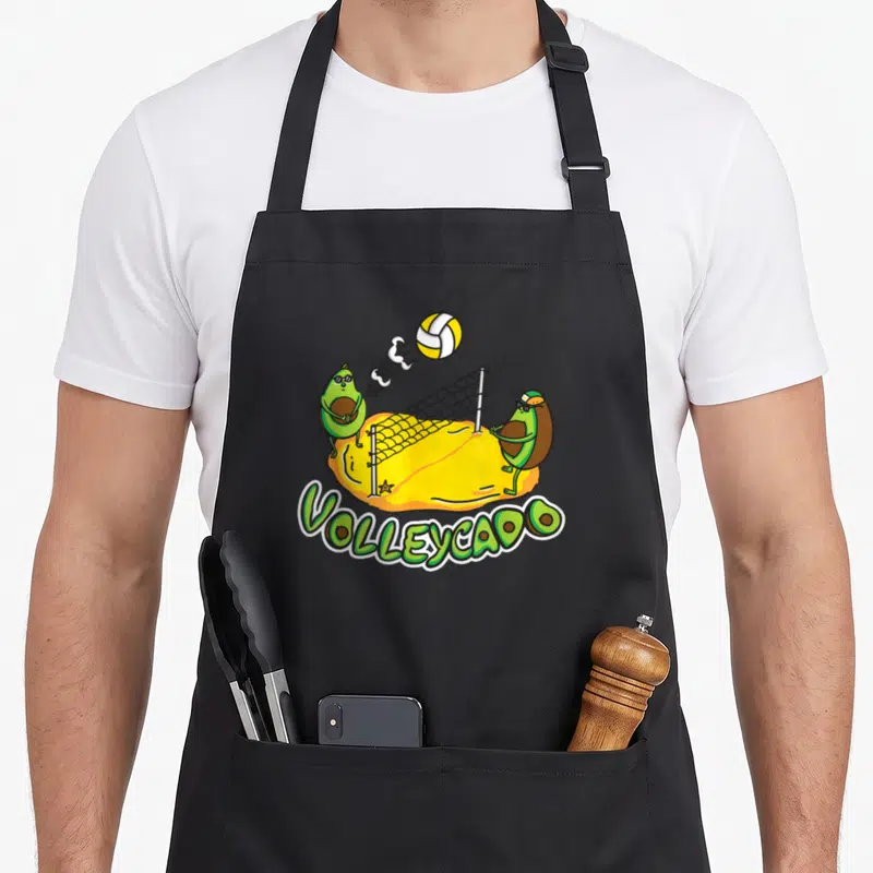 Tablier de cuisine noir avec illustration de deux avocats jouant au volley-ball sur un terrain de sable jaune et le mot Volleycado.