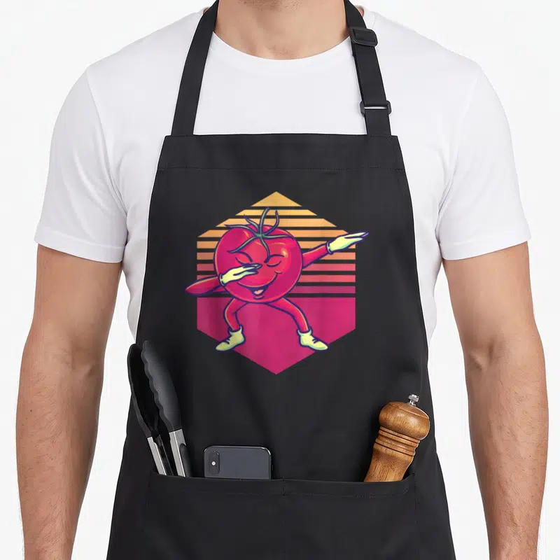 Tablier de cuisine noir avec une tomate rouge anthropomorphique effectuant un mouvement de danse sur fond géométrique coloré.