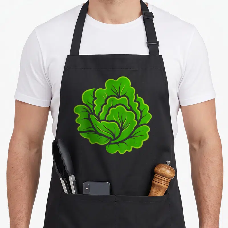Tablier de cuisine noir avec illustration centrale d'une salade légume simple aux feuilles vertes ondulées et contours clairs.