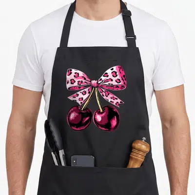 Tablier de cuisine noir avec deux cerises roses et un nœud rose à motifs léopard noir imprimé au centre.