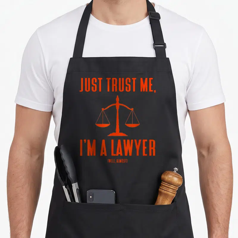 Tablier de cuisine noir avec inscription orange Just Trust Me I'm a Lawyer Well Almost et une balance de la justice au centre.