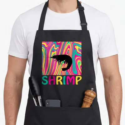 Tablier de cuisine noir avec silhouette de crevette sur fond ondulé multicolore et texte shrimp en bas.