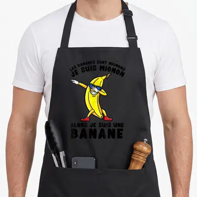 Tablier de cuisine noir avec une illustration de banane en pose de dab portant des lunettes bleues et des chaussures rouges.