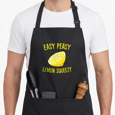 Tablier de cuisine noir avec illustration d'un demi-citron jaune et du texte Easy Peasy Lemon Squeezy en lettres capitales.