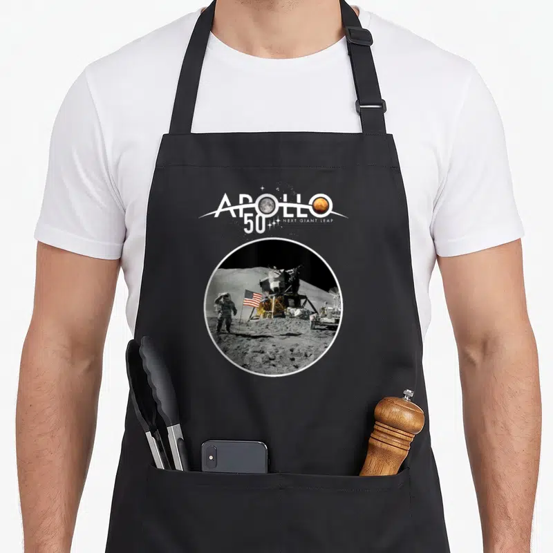 Tablier de cuisine noir avec illustration circulaire Apollo 50 Next Giant Leap et astronaute sur la Lune.