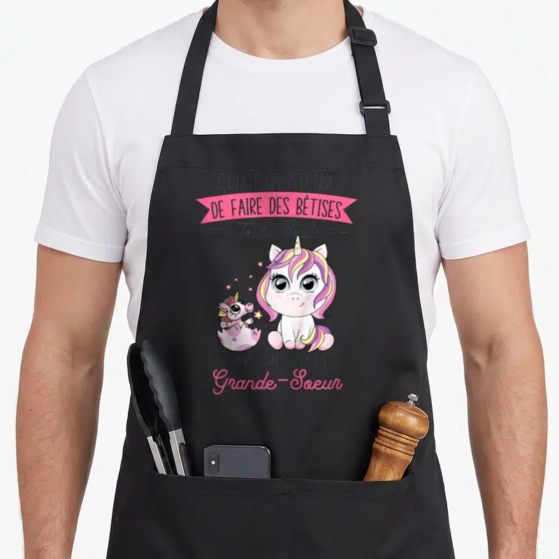 Tablier de cuisine noir avec licorne rose et message humoristique sur l'annonce de grande-sœur