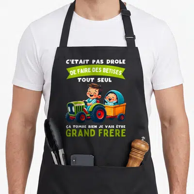 Tablier de cuisine noir avec un garçon au tracteur tirant une remorque et du texte blanc et vert.