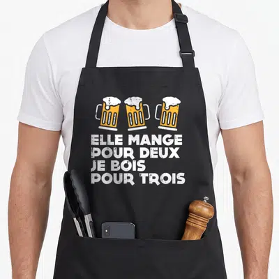 Tablier de cuisine noir avec trois bières et le texte Elle mange pour deux je bois pour trois en blanc.