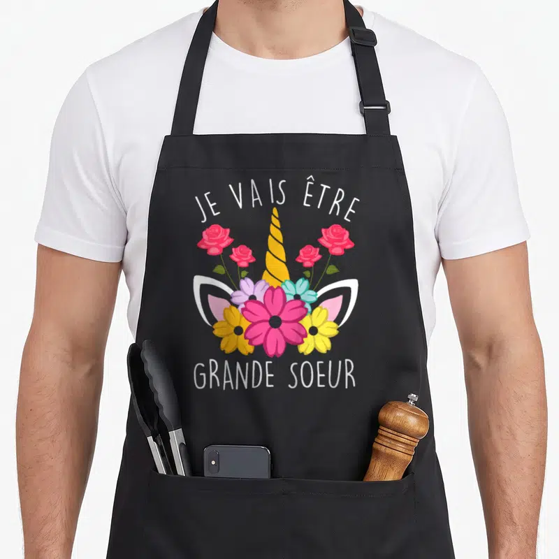 Tablier de cuisine noir avec illustration d'unicorne fleurie et texte Je vais être Future Grande Soeur en blanc.
