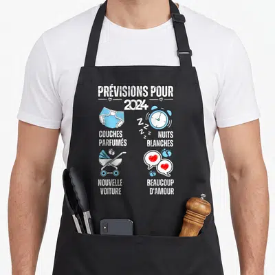 Tablier de cuisine noir avec illustration annonçant des prévisions pour 2024 incluant un biberon et un réveil.