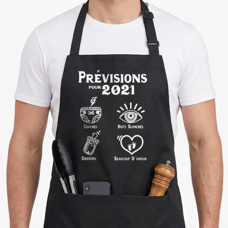 Tablier de cuisine noir avec illustration blanche Prévisions pour 2021 incluant couches, yeux, biberon et pieds dans un cœur.