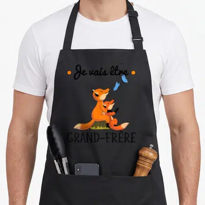 Tablier de cuisine noir avec illustration de deux renards orange et le texte Je vais être grand-frère.
