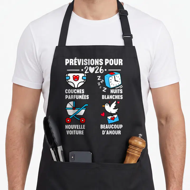 Tablier de cuisine noir avec illustration colorée annonçant les prévisions pour 2026 incluant une poussette et des couches.