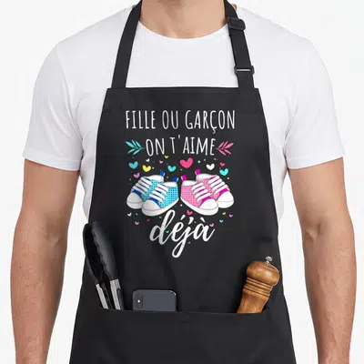 Tablier de cuisine noir avec illustration de baskets roses et bleues et texte Fille ou garçon on t'aime déjà.