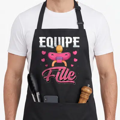 Tablier de cuisine noir avec illustration d'une sucette rose, des cœurs et le texte Equipe Fille en typographie stylisée.