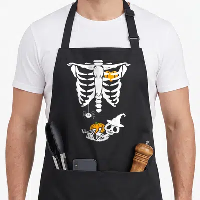 Tablier de cuisine noir avec illustration squelette de maternité, cage à côtes orange et petit crâne au chapeau de sorcière.