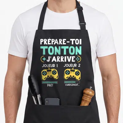 Tablier de cuisine noir avec texte Prépare-toi Tonton J'arrive et deux manettes de jeu vidéo jaunes Joueur 1 et Joueur 2.