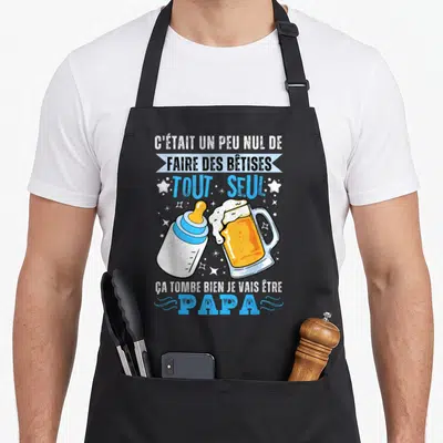 Tablier de cuisine noir avec illustration d'un biberon et d'une bière et texte humoristique sur la future paternité.