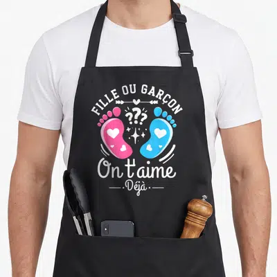 Tablier de cuisine noir avec l'inscription Fille ou Garçon et deux petits pieds roses et bleus ornés de cœurs.
