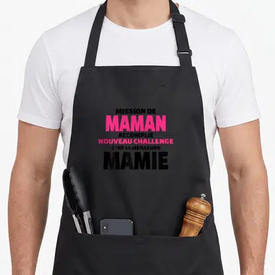 Tablier de cuisine noir avec inscription Mission de Maman Accomplie Nouveau Challenge Être la Meilleure Mamie en rose et noir.