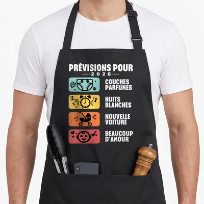 Tablier de cuisine noir avec illustration colorée listant les prévisions pour 2026 incluant couches, nuits blanches et poussette.