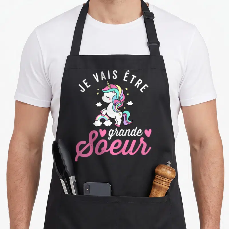 Tablier de cuisine noir avec illustration d'un poney arc-en-ciel et texte Je vais être grande soeur 2024 en lettres roses et blanches.