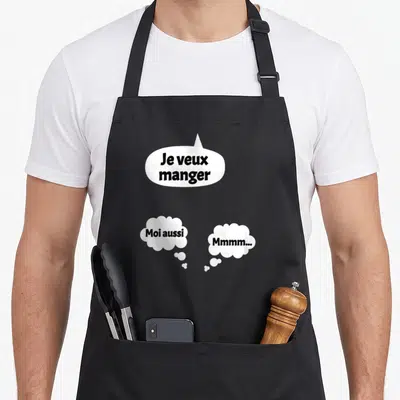Tablier de cuisine noir orné de trois bulles blanches contenant le texte Je veux manger Moi aussi et Mmmm en typographie noire.