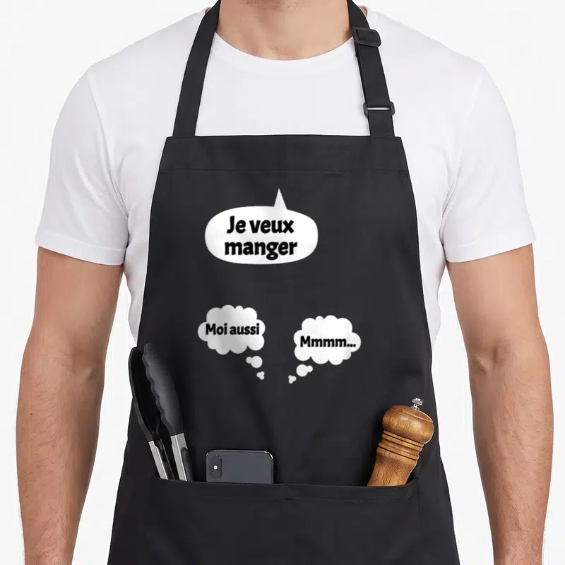 Tablier de cuisine noir orné de trois bulles blanches contenant le texte Je veux manger Moi aussi et Mmmm en typographie noire.
