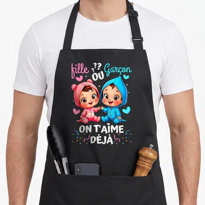 Tablier de cuisine noir avec illustration de bébés rose et bleu tenant la main sous le texte On T'Aime Déjà.