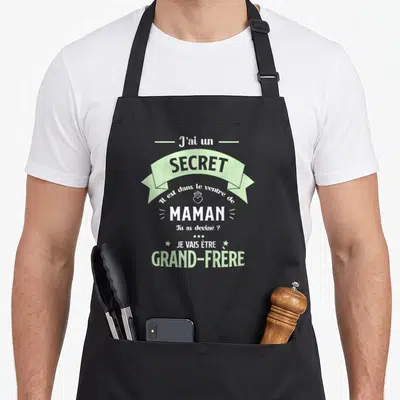 Tablier de cuisine noir avec inscription blanche et vert menthe annonçant la naissance d'un grand-frère dans un style bannière.