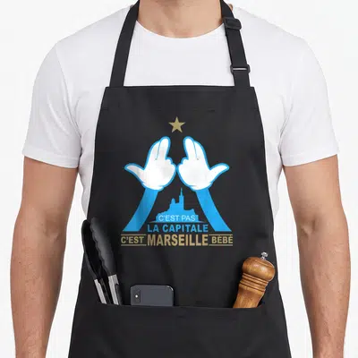 Tablier de cuisine noir avec illustration des mains marseillaises et texte C'est Pas la Capitale C'est Marseille bébé en bleu et doré.